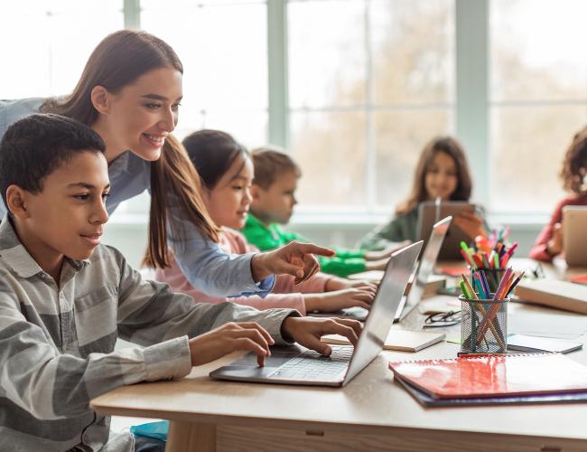 Students on computers with teacher helping